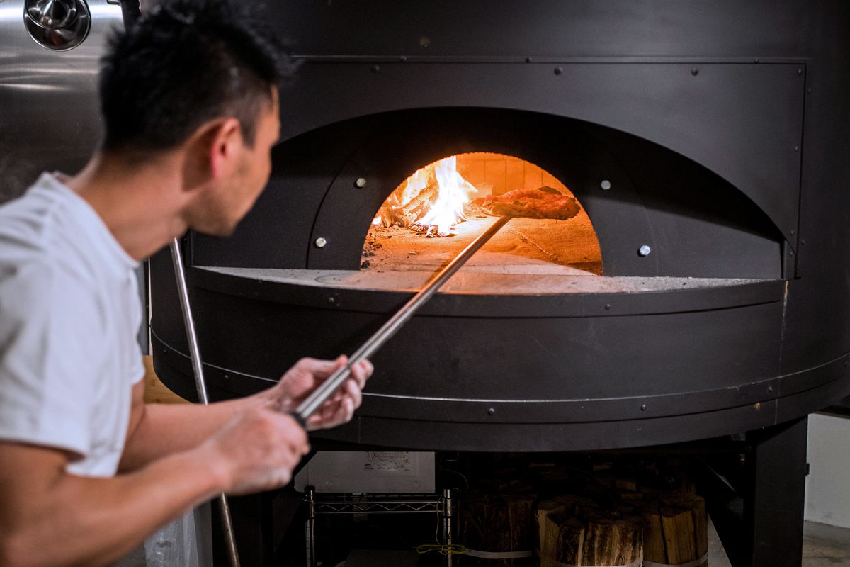 A worker turns a pizza inside of a steel oven in Tokyo.
