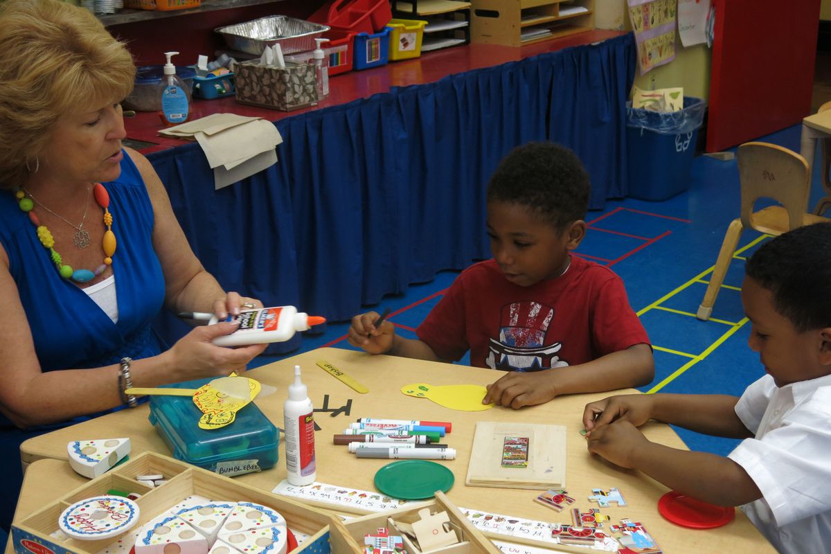 A pre-K teacher at New Bridges Elementary works with two students in their classroom's "math center."