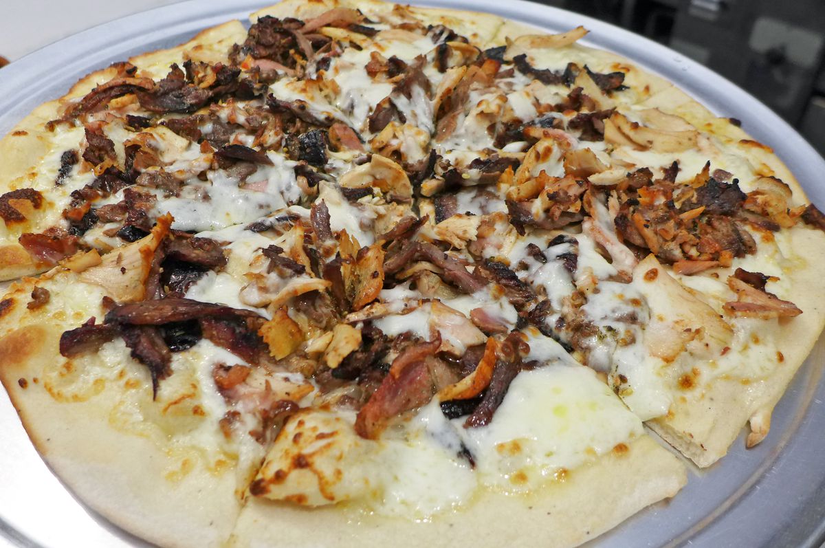 A pizza crust with melted white cheese and shards of poultry and meat.
