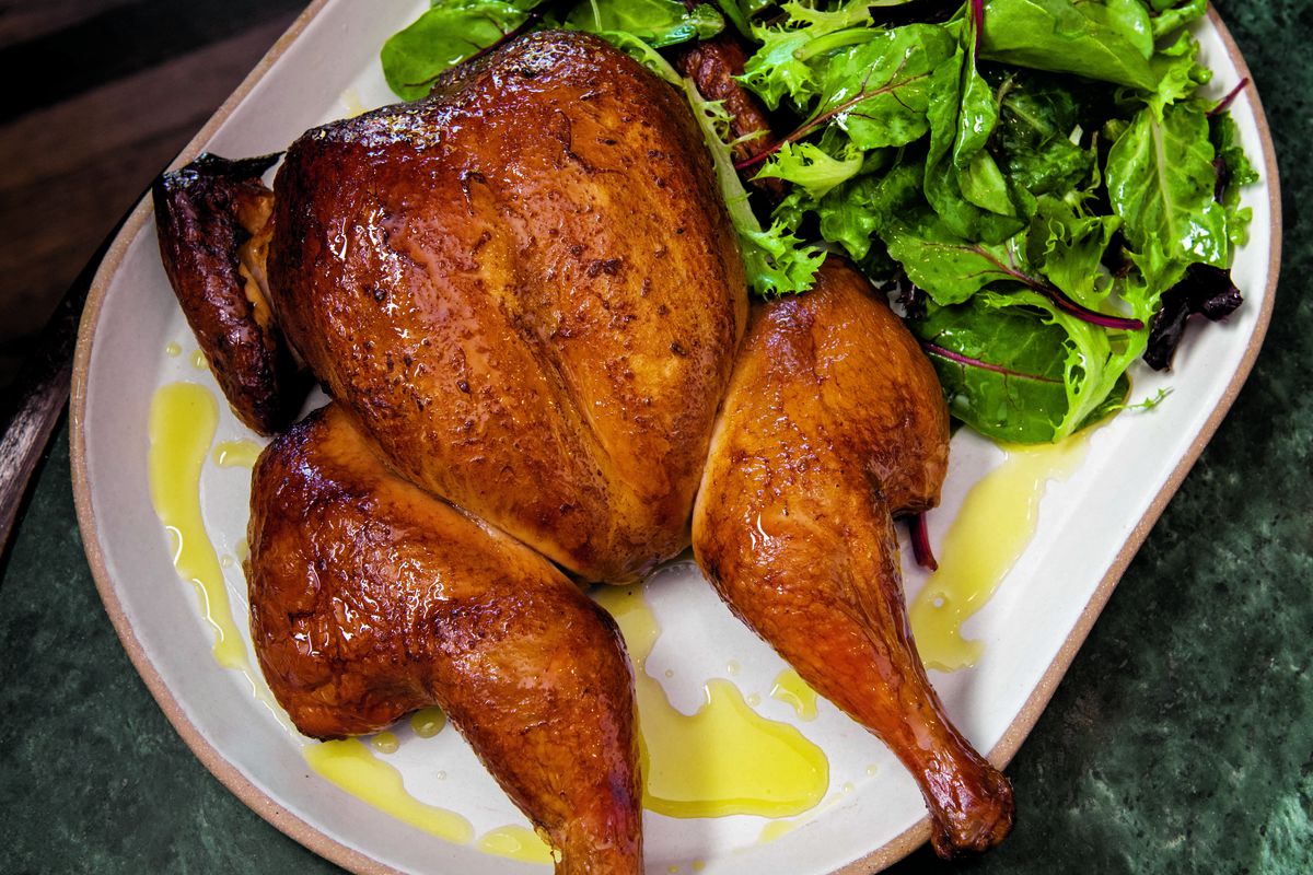 A plate of a roasted chicken with greens on a plate.