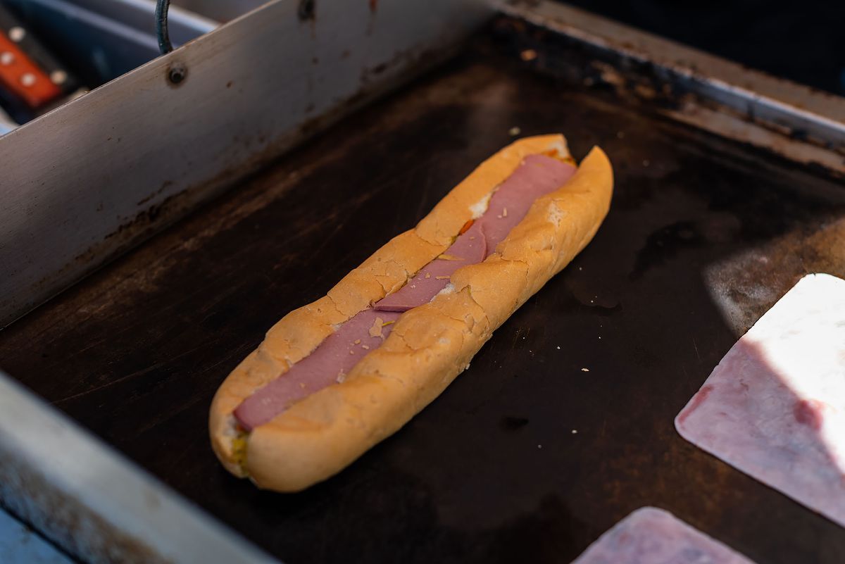 A long, thin sandwich sits on a warm griddle in the shade.