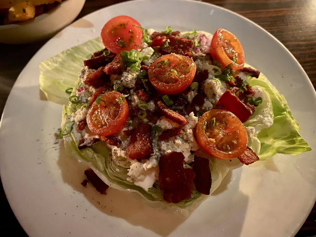 A wedge of iceberg lettuce topped with blue cheese, bacon, and tomatoes.