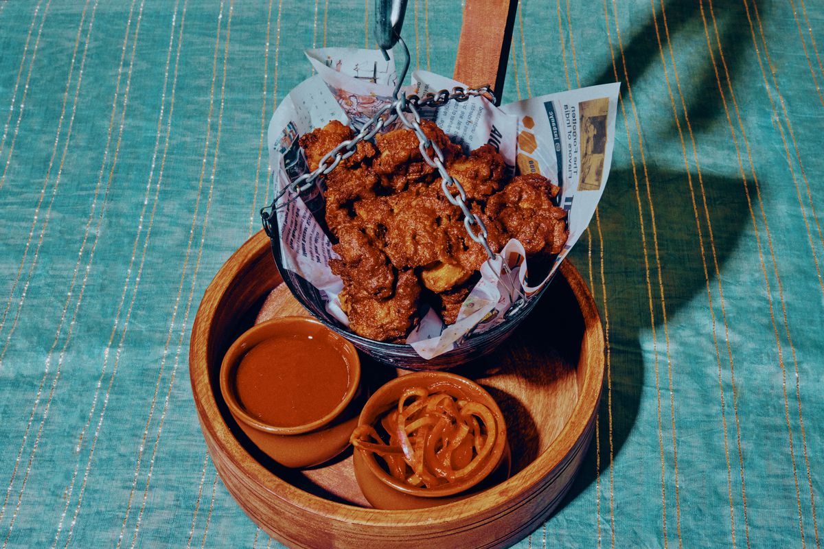A basket of fried chicken hangs from a hook beside dippings sauces and pickled onions.