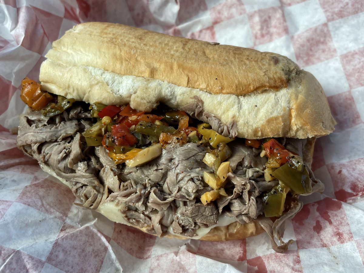 An overflowing sandwich of shredded beef and fixings, on wax paper wrapping.