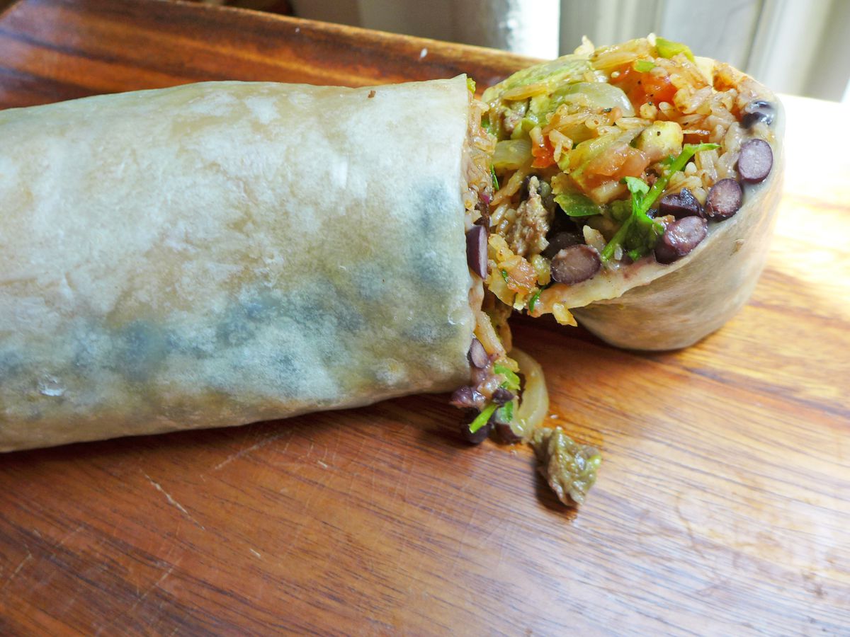 Two halves of a torpedo-shaped burrito, filled with black beans, rice, cilantro, and what appears to be pico de gallo