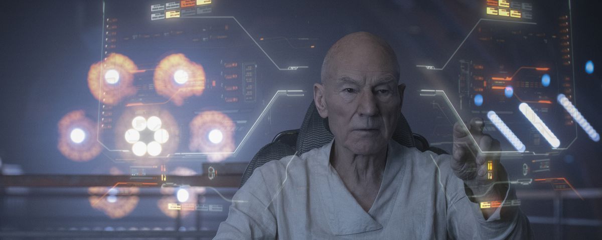 Patrick Stewart as Jean-Luc Picard pilots a ship, surrounded by virtual heads-up displays