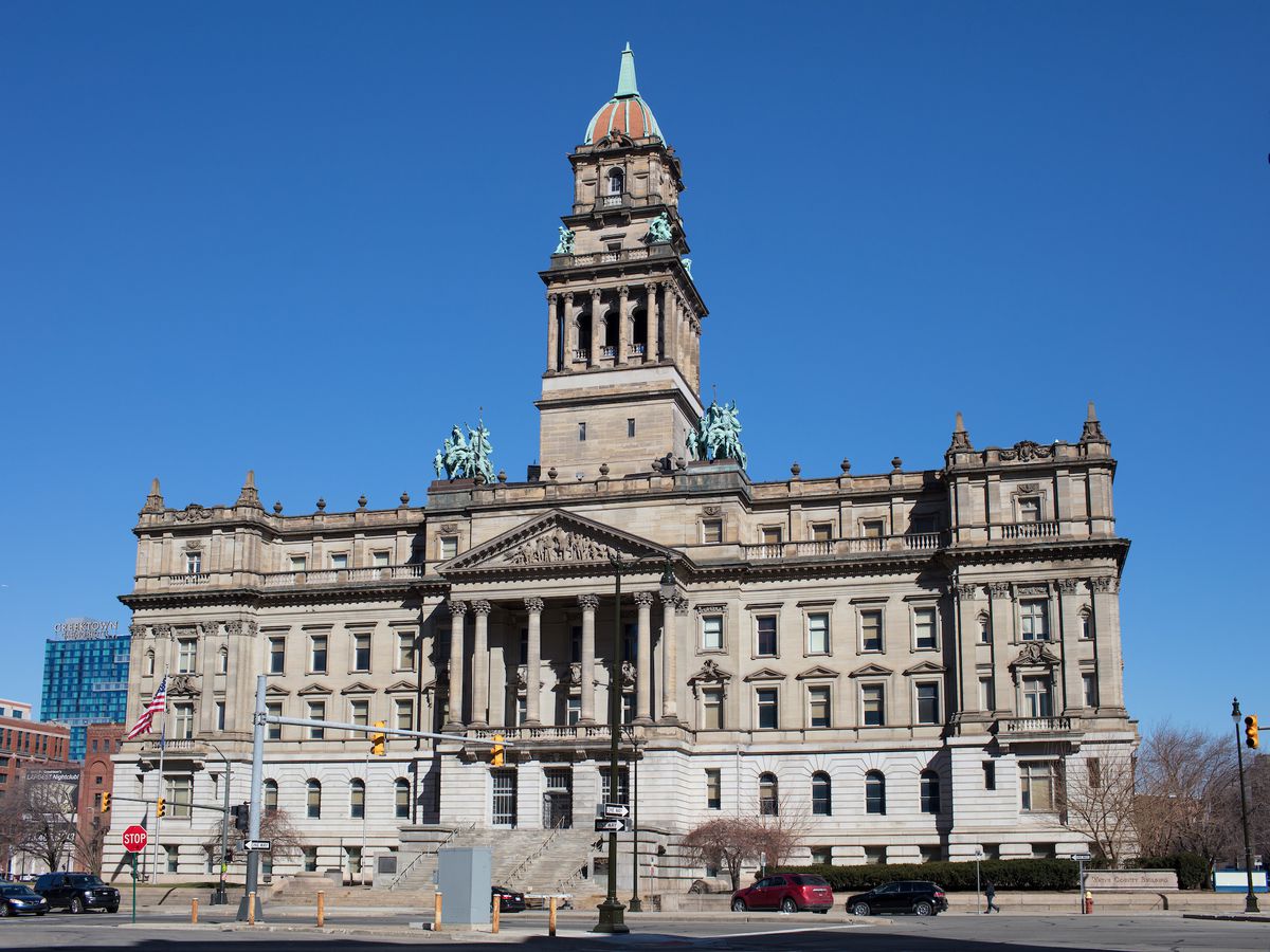 A Renaissance Revival stone courthouse with columns at the front entrance and copper statues on the roof. 