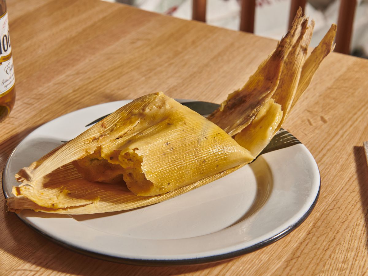 A yellow tamal sits on a corn husk on a white plate