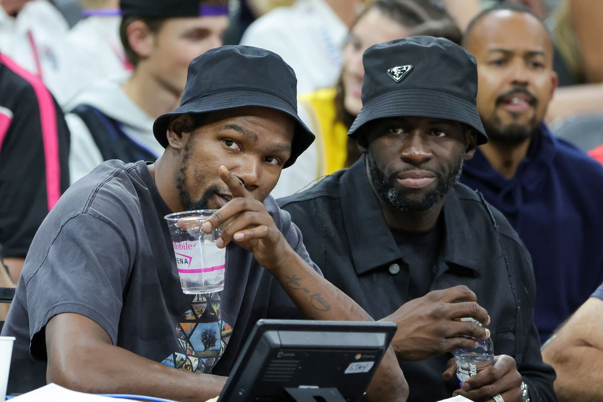 Kevin Durant and Draymond Green smiling and sitting next to each other in the stands of a game.