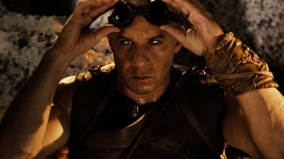 Riddick (Vin Diesel) lifting his goggles to reveal his glowing eyes in Riddick (2013).