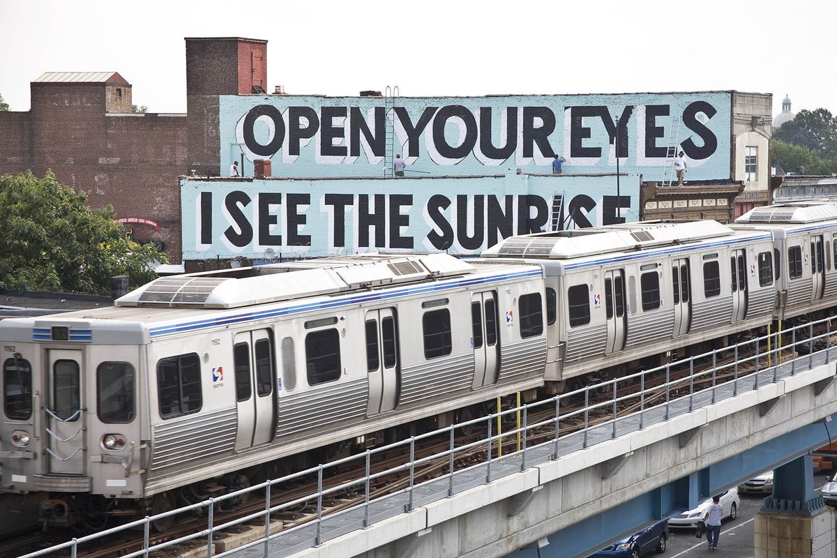 a steve powers mural that says open your eyes i see the sunrise in front of a philadelphia skyline
