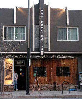 The exterior of a beer bar with dark wooden siding and a sidewalk in front.