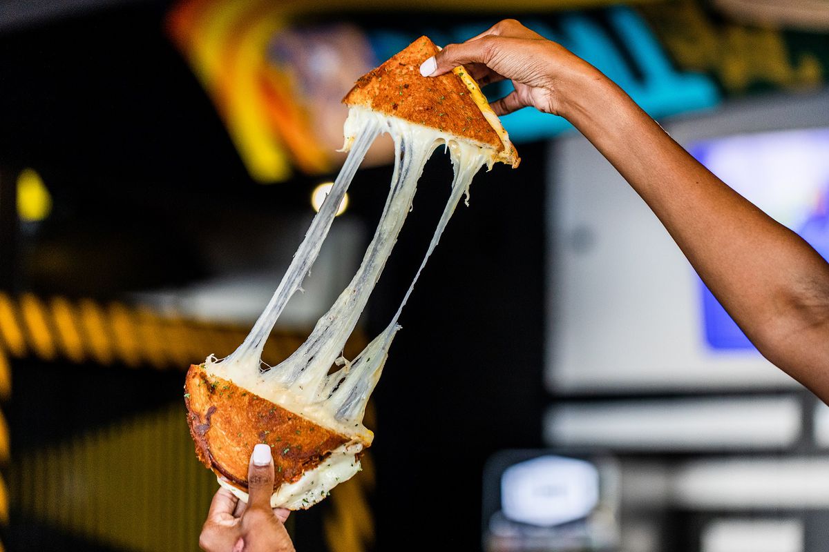 A person stretches the gooey cheese from two sides of a grilled cheese sandwich.