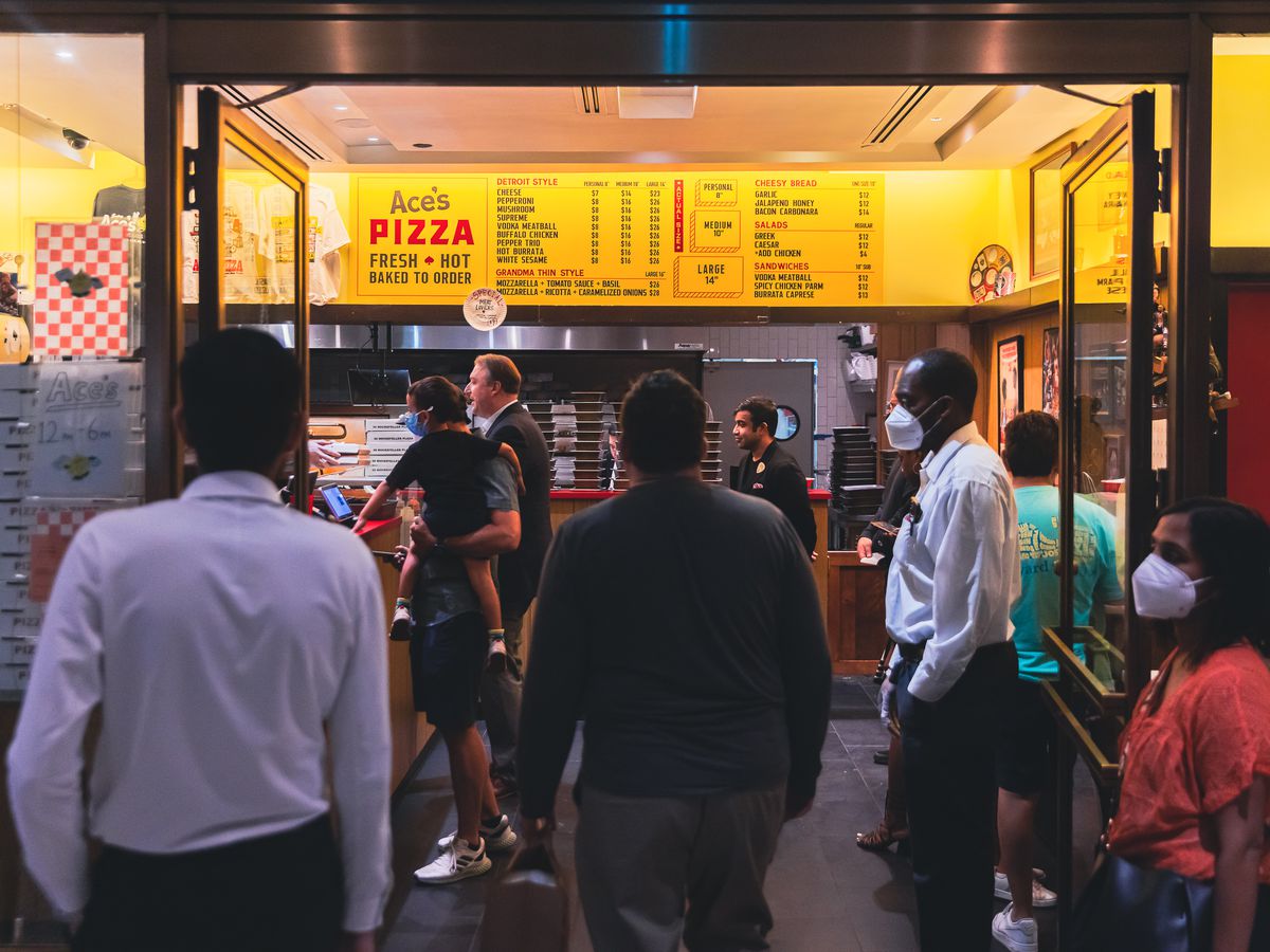Customers wait for their orders around the counter of a pizzeria, Ace’s Perfect Pizza.