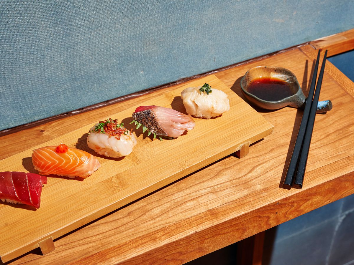Different pieces of fish lined up on a long wooden tray with a pair of black chopsticks placed at the end