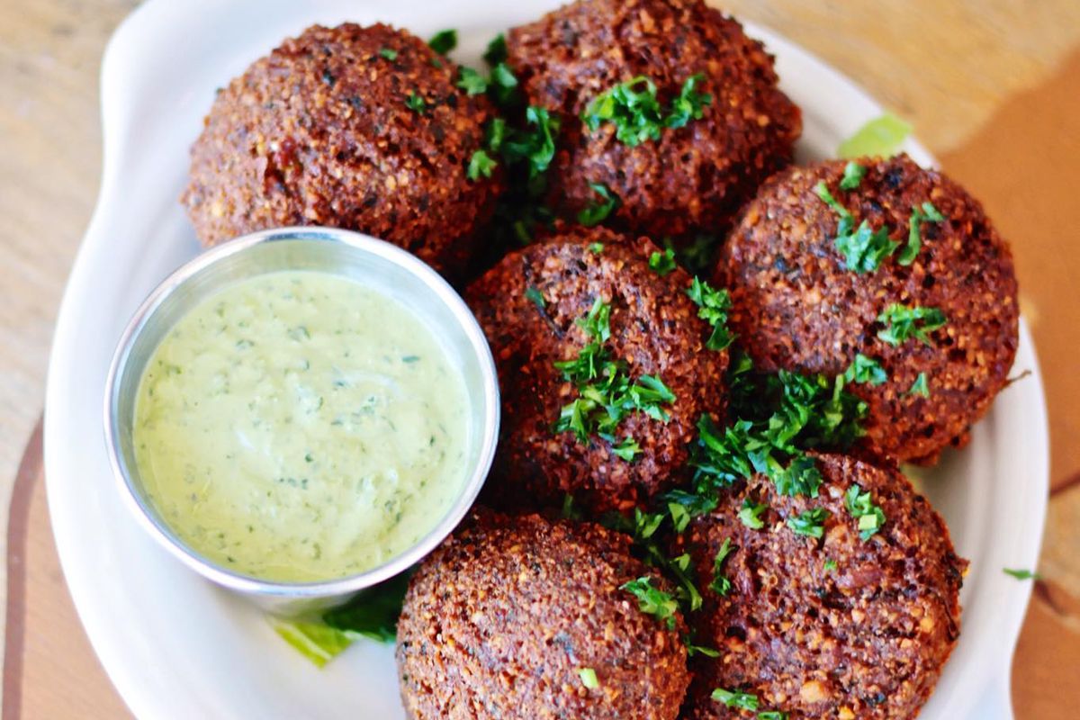 A bowl of falafels and a container of a light green sauce.