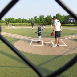 A young batter takes a swing as a father who's a coach supervises at a youth baseball game in Buffalo Grove, Ill. on Monday June 10, 2013. Earlier in the month, park district officials in the Chicago suburb posted signs asking parents to behave and keep the games in perspective. 