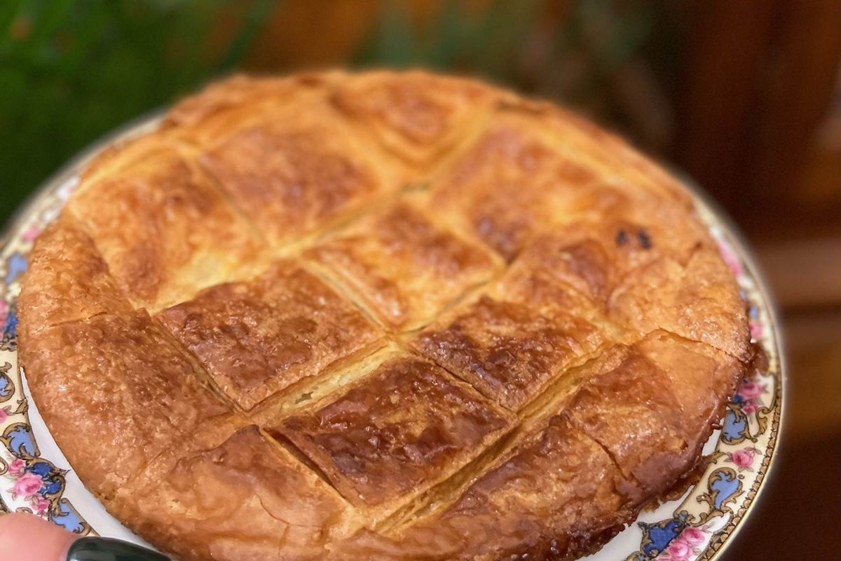 person with dark green nails holding plate with a kouign amann (circular pastry).