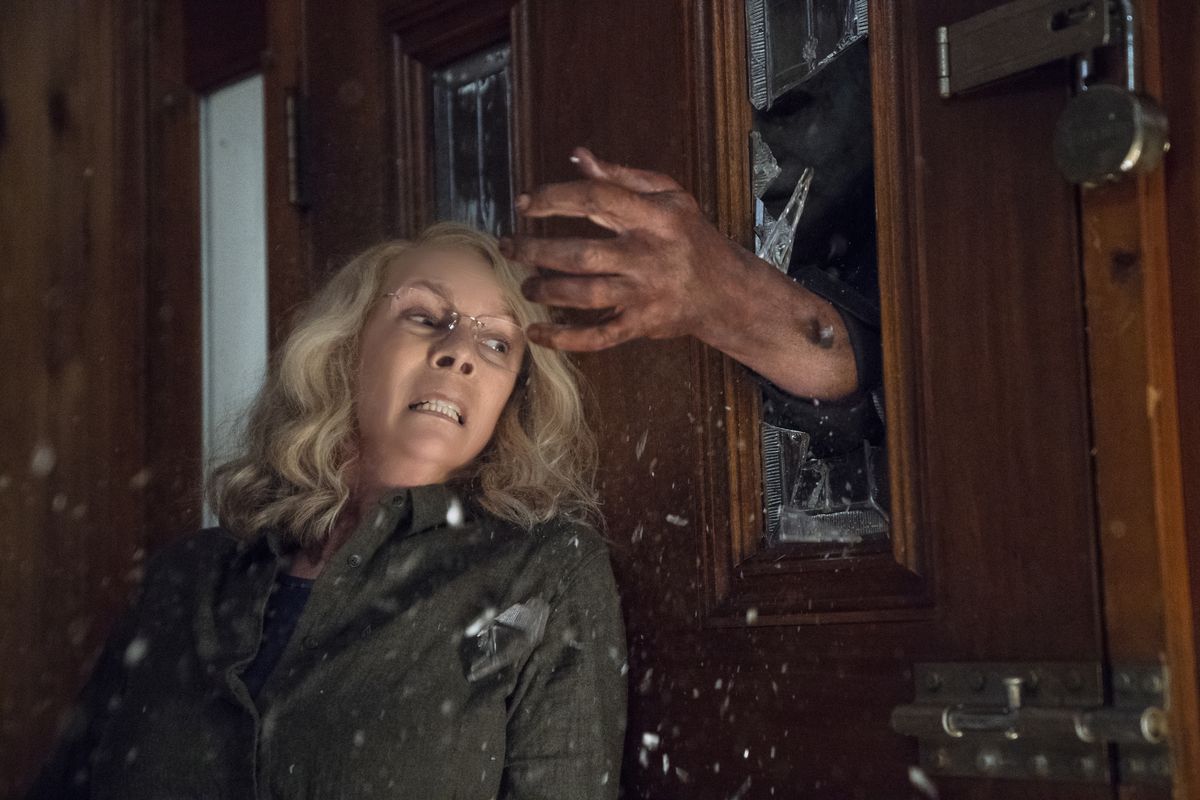 Laurie Strode (Jamie Lee Curtis) dodging Michael Myers’s hand as it comes through the door in the 2018 film Halloween.