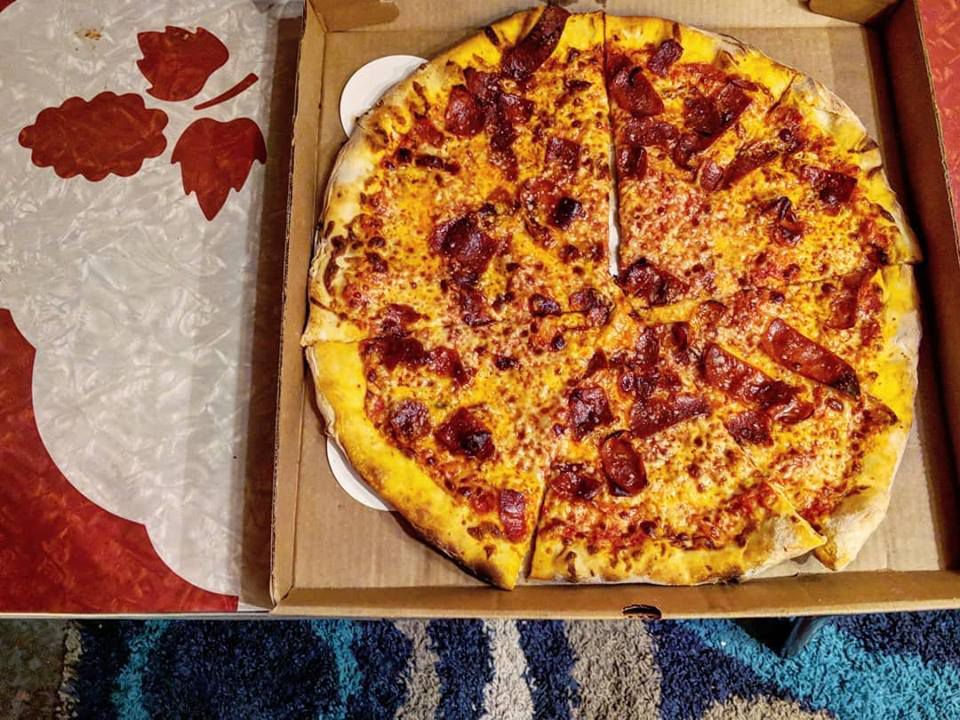 Overhead view of a pepperoni pizza in a takeout box on a red and white table.
