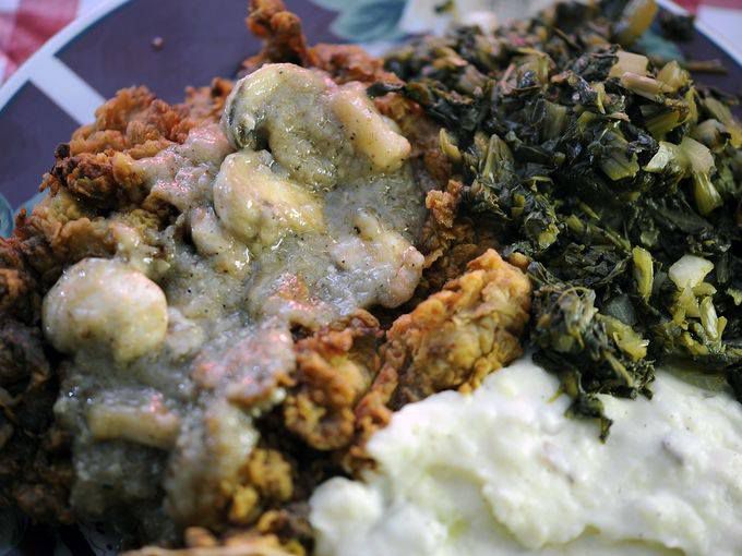 A closeup of fried food with gravy and greens.