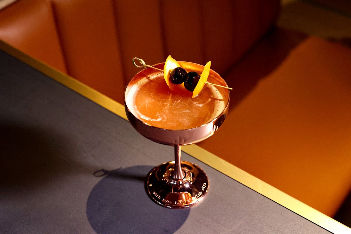 The Warwick’s sidecar royale cocktail in a brass glass, garnished with two cherries and orange peels.