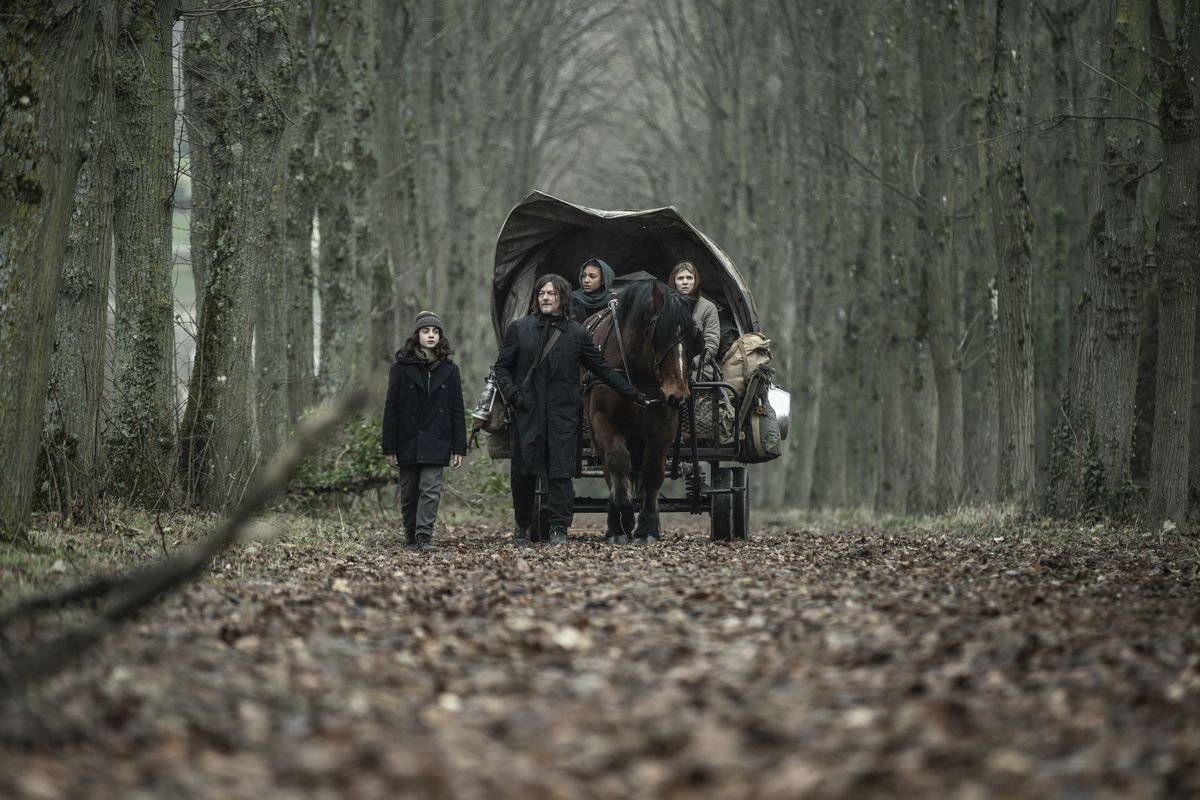 Daryl Dixon (Norman Reedus) walking with his found family through the French forest, pulling along a horse with a wagon