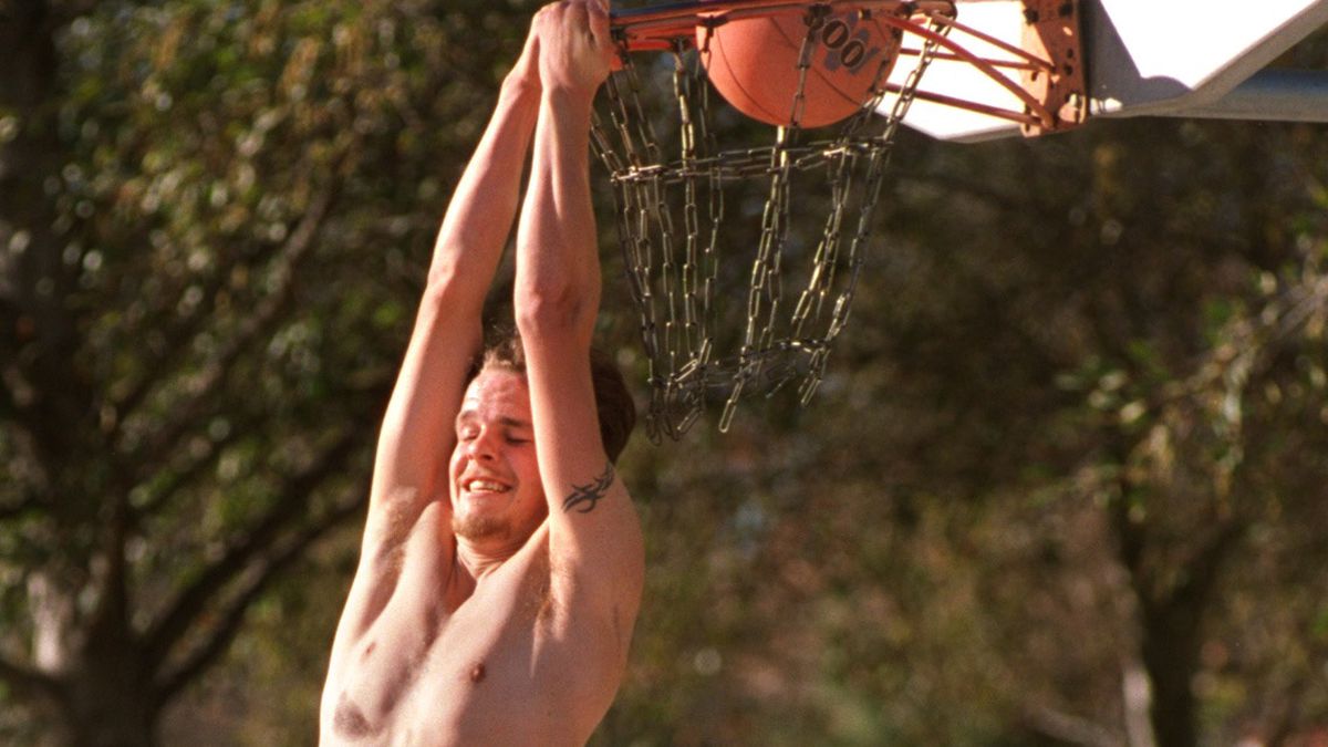 Tim McNees, 21, goes up for a reverse slam dunk while playing basketball on outdoor court at Rancho