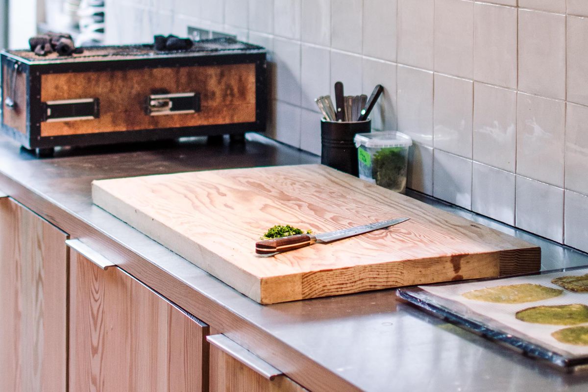 A chopping board with a single knife on it in the foreground; in the background, a konro grill and white tiles.