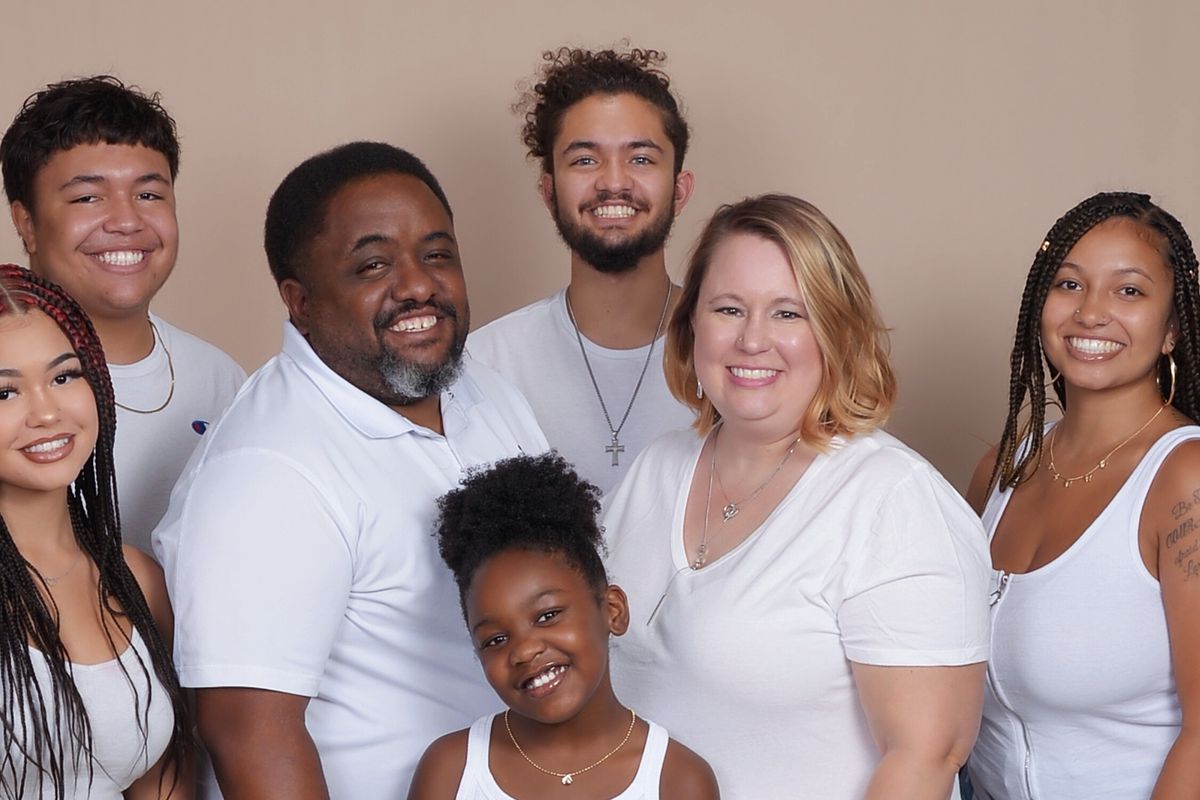 A family portrait Vernon Jones Jr., his wife, and five children. They are all wearing white shirts and smiling at the camera.