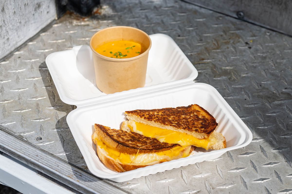 A toasted grilled cheese with side of soup on a food truck step.