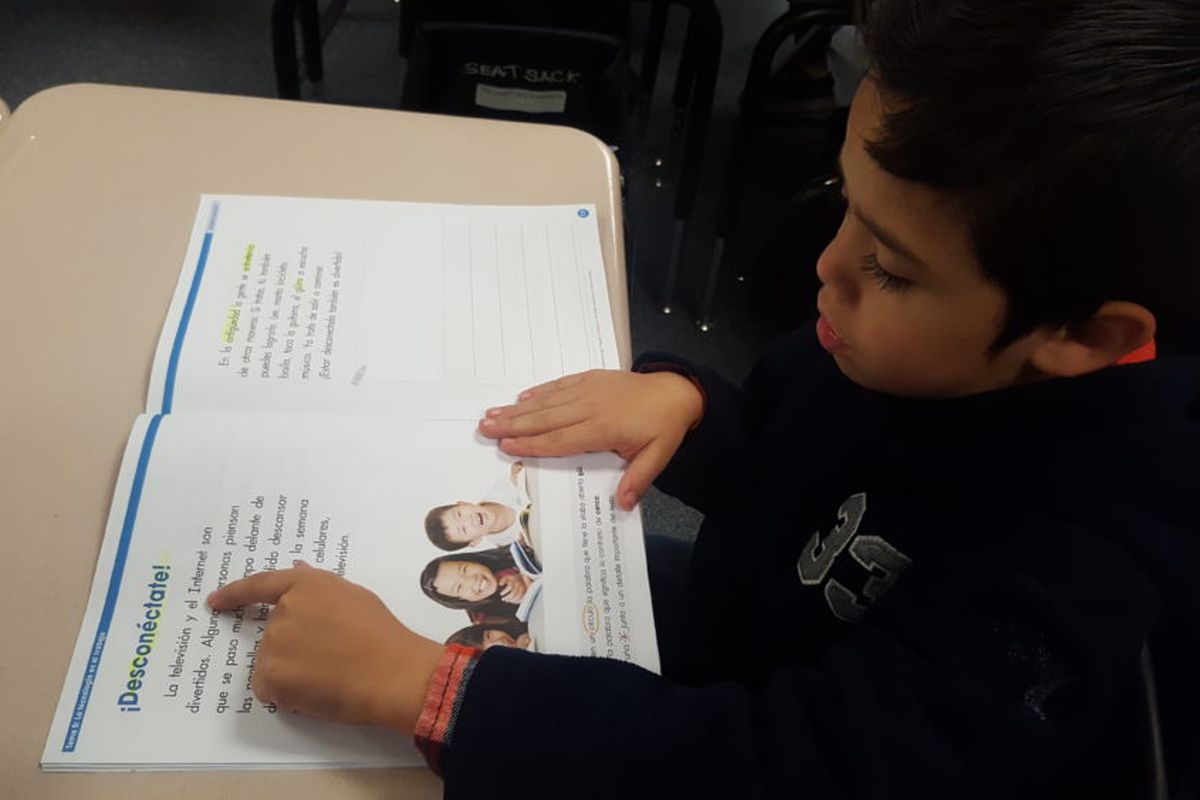 A first-grade student uses his finger to guide himself as he reads in Spanish in a biliteracy classroom in Adams 14.