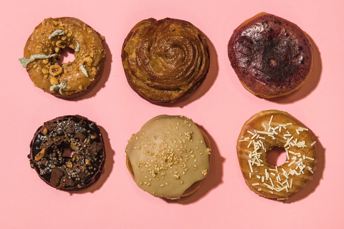 Six doughnuts are laid out in two rows of three on a pink background