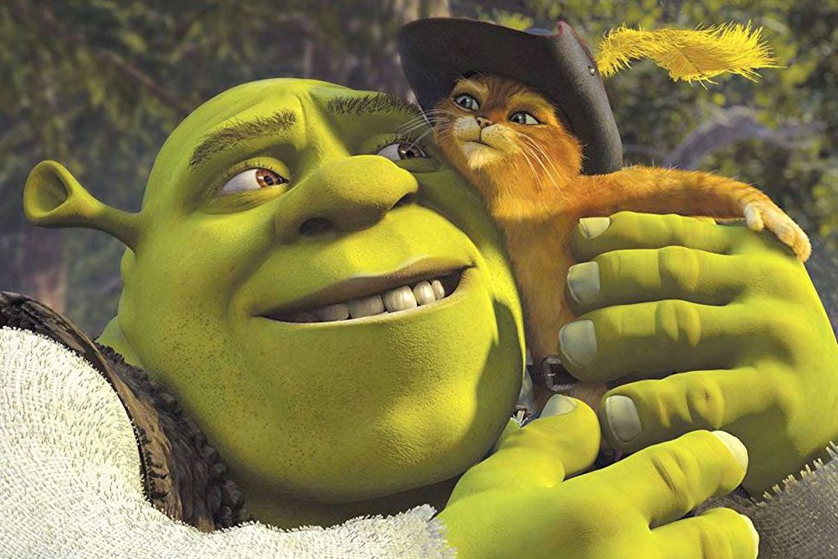Shrek, a green ogre, gives Puss in Boots, an orange anthropomorphic cat wearing a hat, a hug