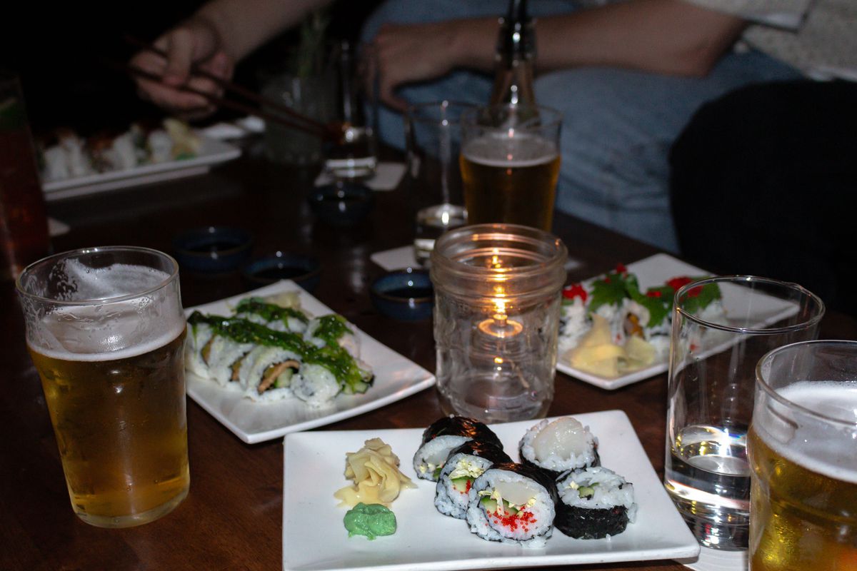 A table with plates of sushi and glasses of beer.