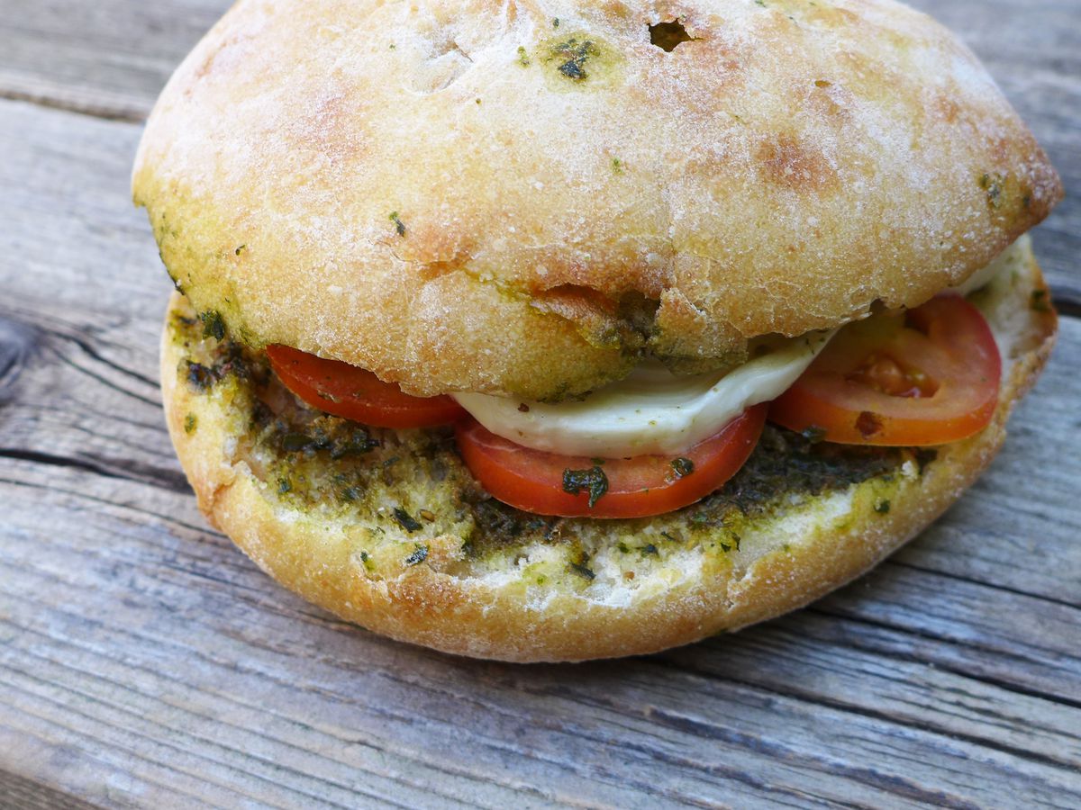 A round sandwich with mozzarella, tomato, and pesto on a wooden picnic table surface.