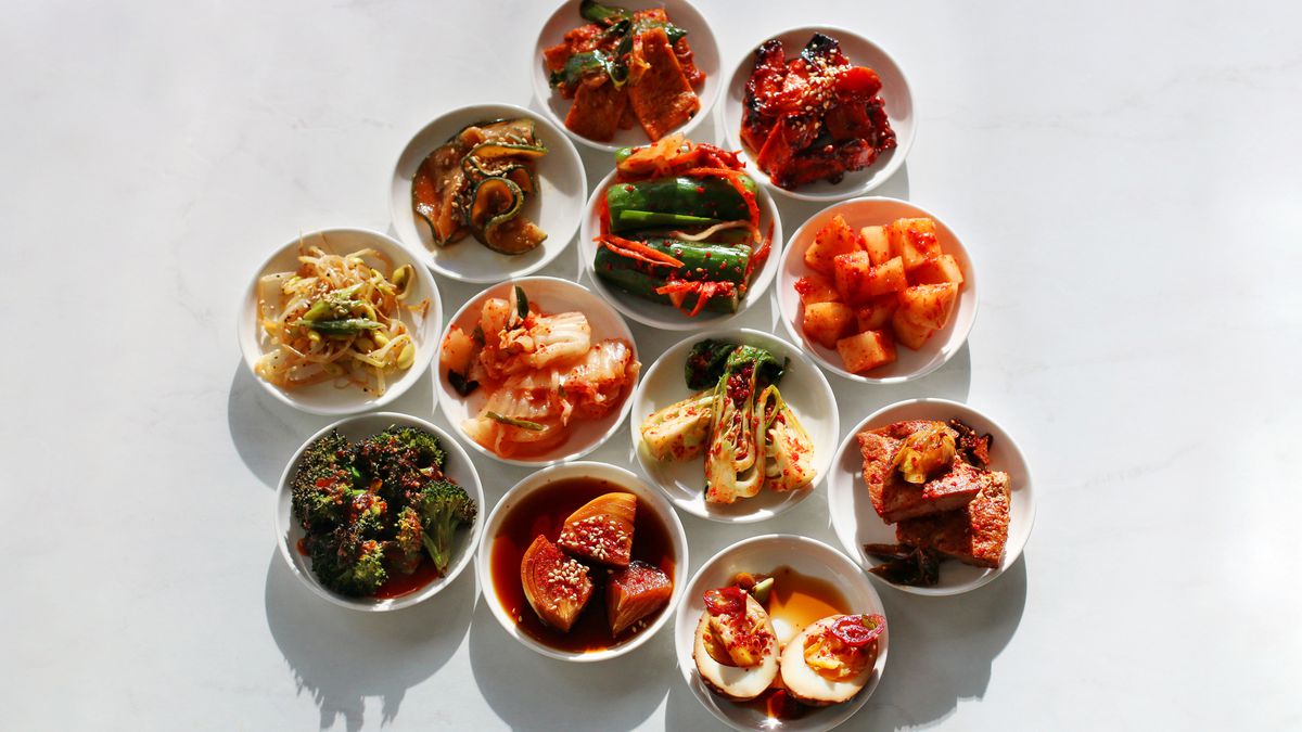 A variety of vegetable banchan in small white plates, including kimchi, egg, broccoli, and bean sprouts.