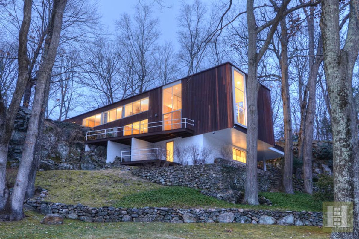 Redwood-clad rectangular volume with glass expanses cantilevers over steep rocky site. 