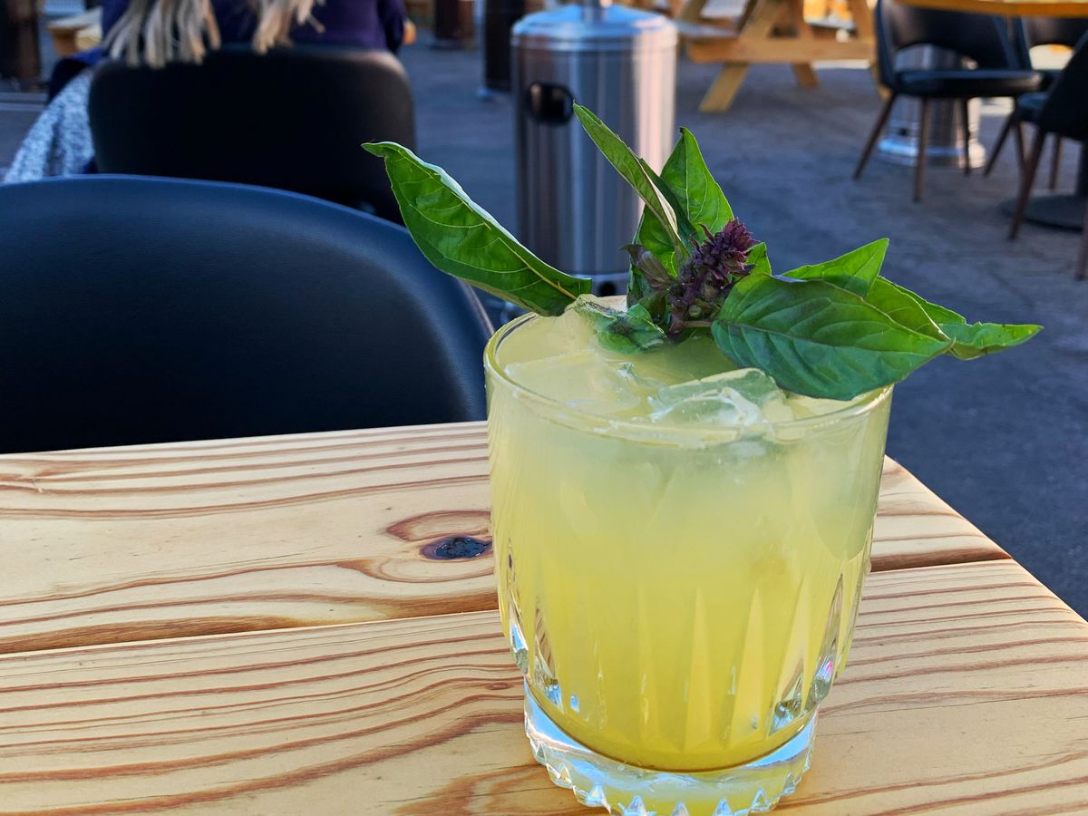 A yellow cocktail topped with a bunch of thai basil