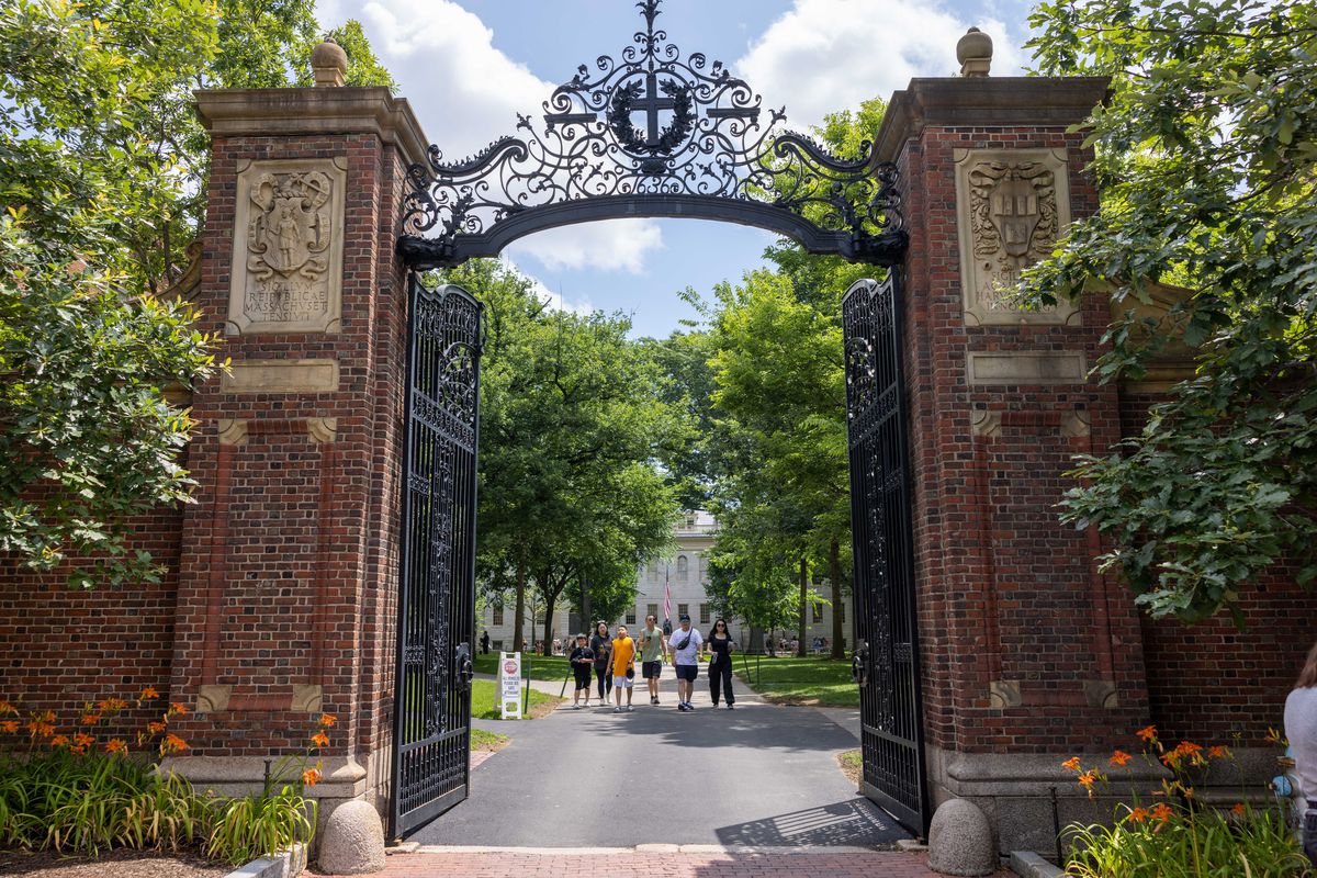 People in the distance viewed through the ornate iron gate at Harvard