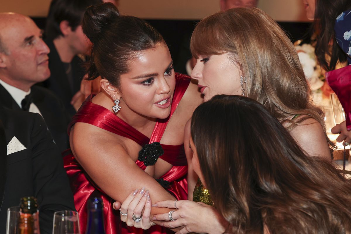 Selena Gomez leaning in to speak to Taylor Swift at the Golden Globes award show.