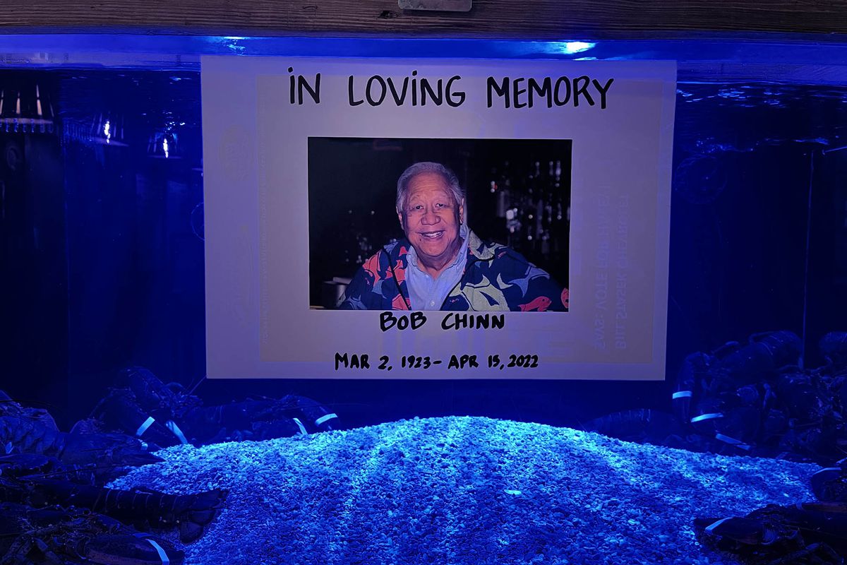 A fish tank with a sign taped to the front with a picture of an old man in a shirt printed with fish.