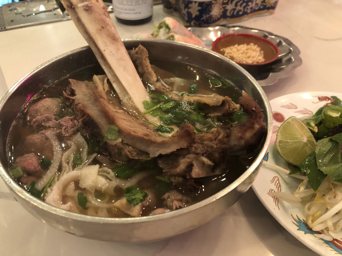 A big metal bowl of pho topped with a whole beef rib. 