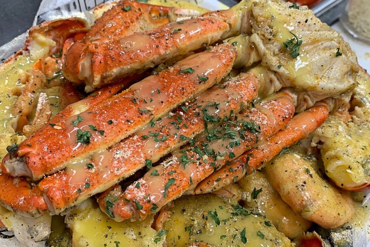 a big bowl of boiled seafood topped with a buttery sauce, including crab legs, corn, shrimp and more