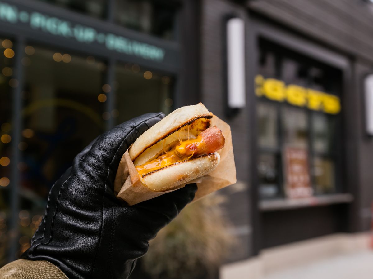 An egg, ham, and cheese breakfast sandwich held in a black-gloved hand.