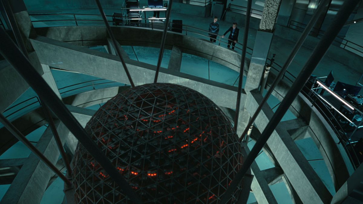 a man and woman look over the edge of a circular building to see Rehoboam, a spherical AI glowing red