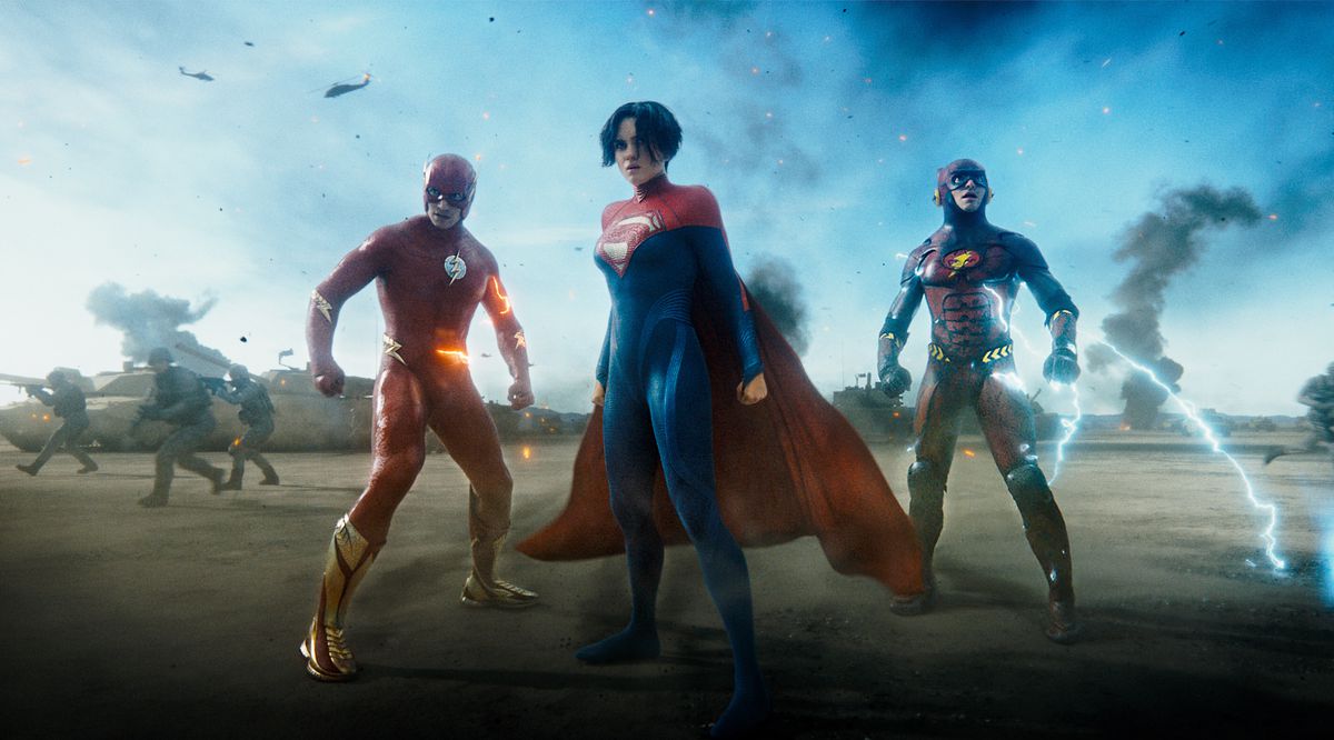 Supergirl stands in front of Barry Allen and his younger self, each in their own Flash costume, on a battlefield surrounded by Kryptonian soldiers in the film The Flash
