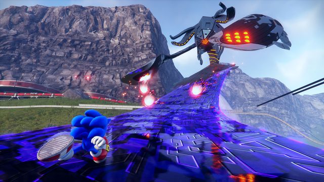 Sonic the Hedgehog races up the sleek limb of a giant one-eyed metal creature called a Titan in an open-world area bordered by a mountain ridge in a screenshot from Sonic Frontiers