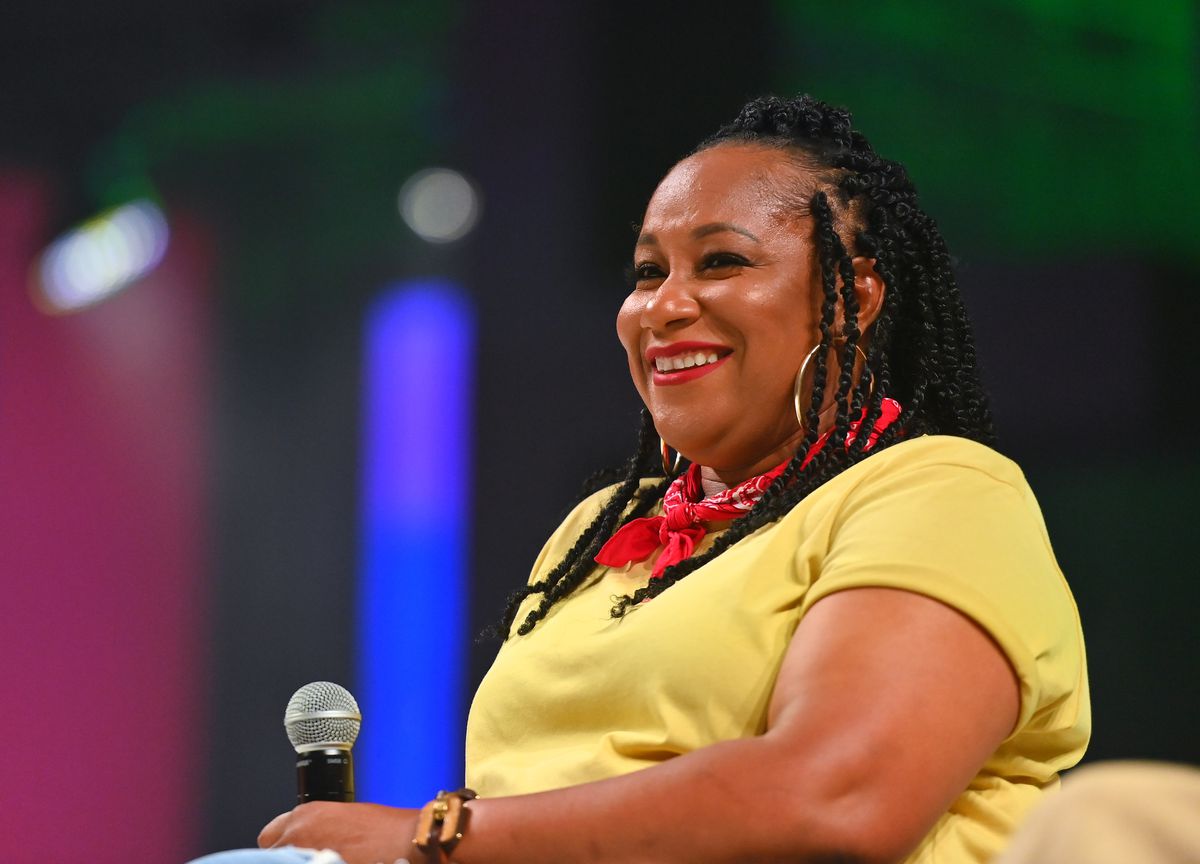 A Black woman chef wearing a yellow shirt speaks at a conference.