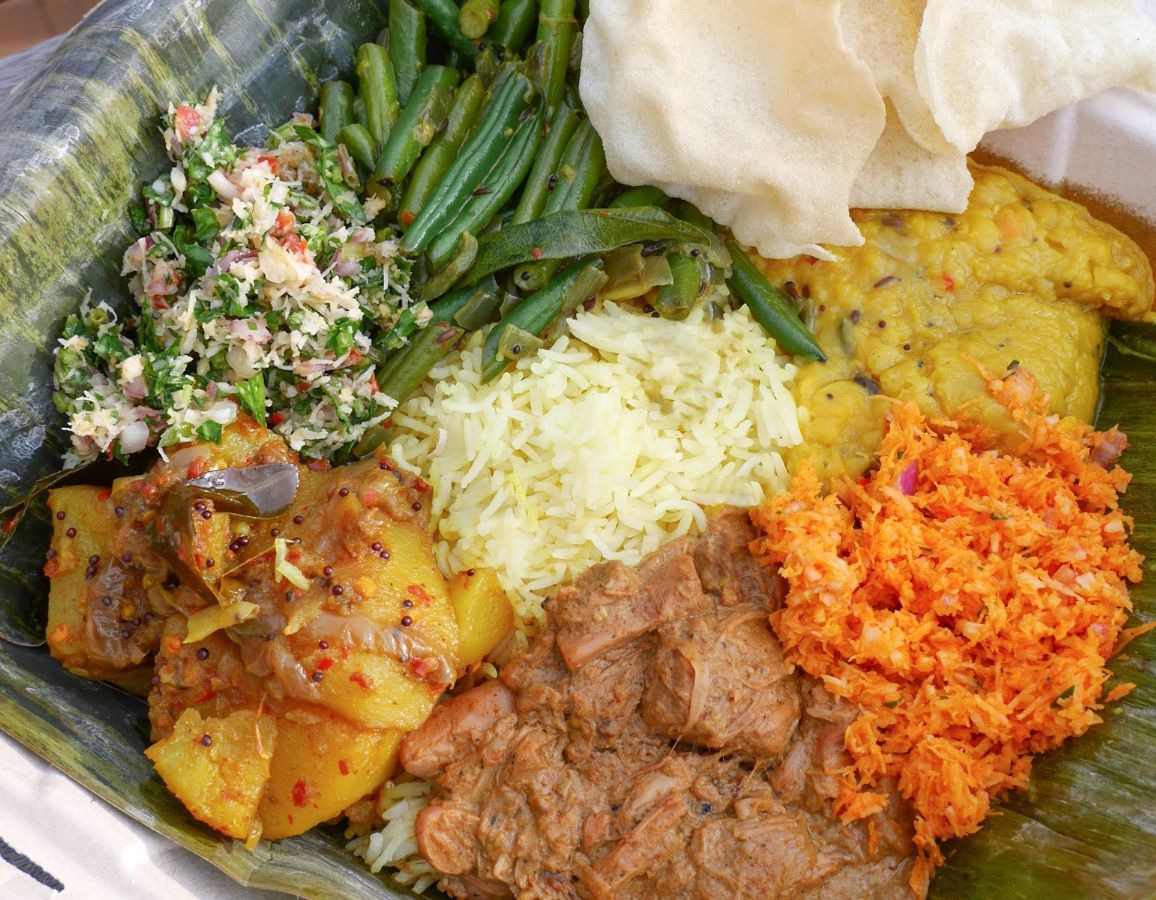 A photo of Mirisata Sri Lankan rice and curry plate, with green beans, rice, potatoes, coconut, and more.